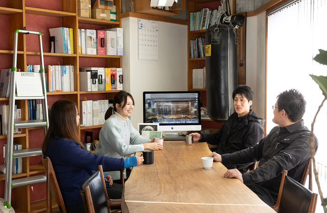 「三輝」の看板が掲げられた建物の前で、作業着姿のスタッフを含む7人の社員が並んで写る集合写真